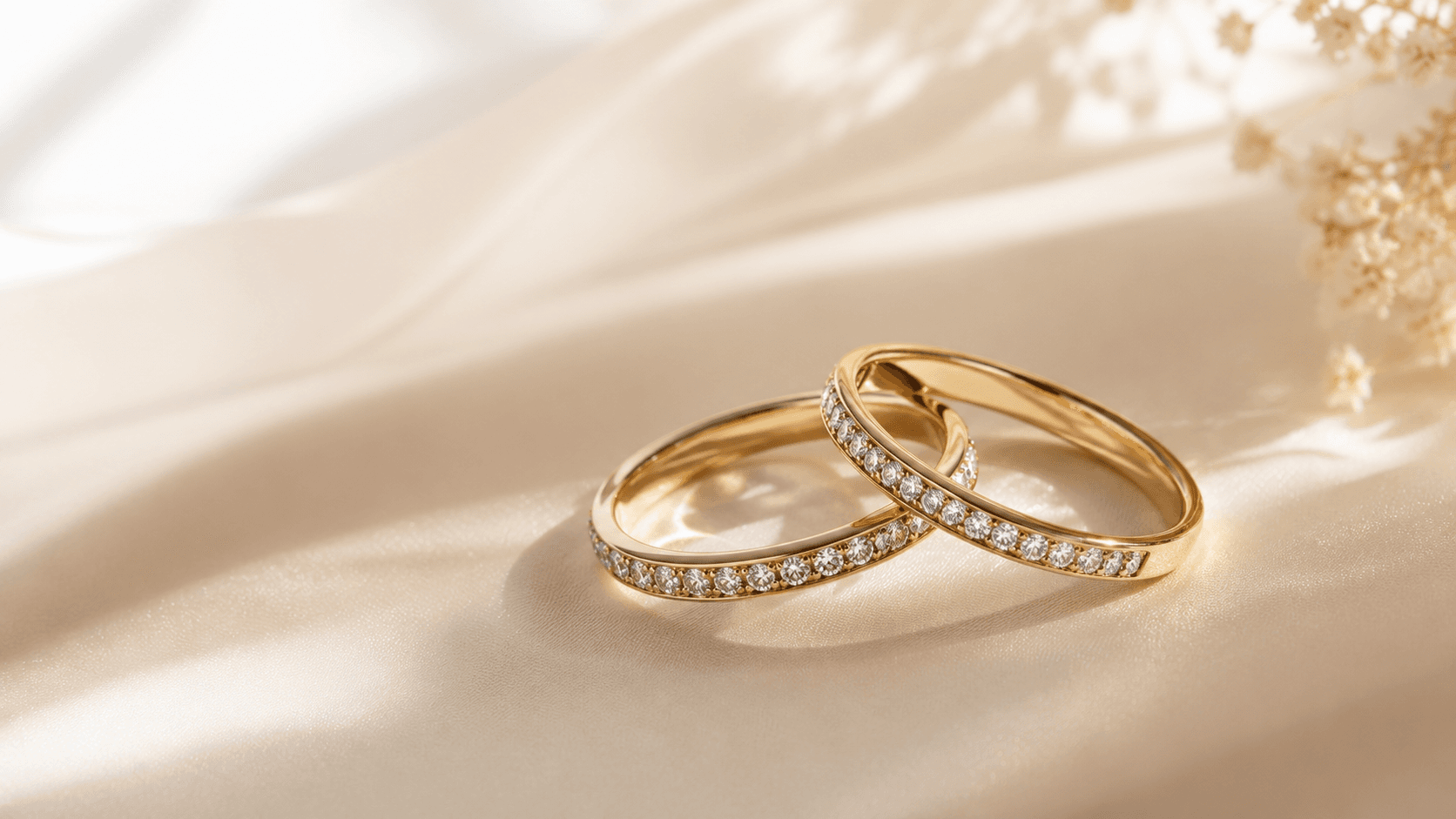 Two gold diamond eternity rings on soft cream fabric with white flowers